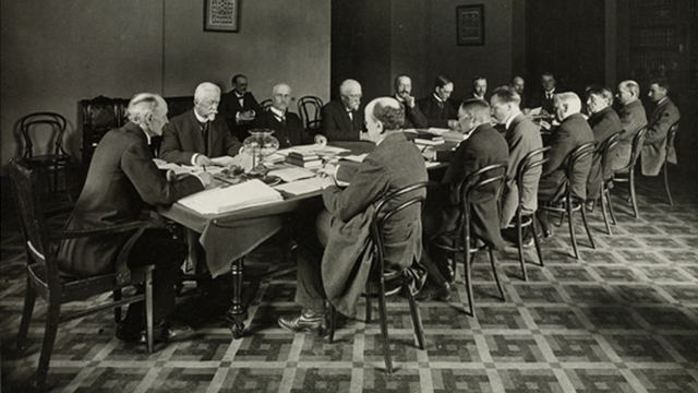 Grundlagsutskottet sammanträder i Ständerhuset 1918. I ändan på bordet ordföranden professor K.J. Ståhlberg, friherre R.A. Wrede, utskottets sekreterare Hjalmar Kahelin (vid det bakre bordet), professor Ernst Estlander, professor G.G. Rosenqvist, prost A.O. Wuorimaa, författare Santeri Alkio, redaktör Antti Juutilainen, lärare J.P. Kokko, redaktör Eero Erkko, doktor Tekla Hultin (vid ändan av bordet), jordbrukare P. Pennanen, jordbrukare E. Tukia, prost W. Malmivaara, prost F.W. Bergroth, jordbrukare O. Rantasalo, jordbrukare J.E. Antila, professor Lauri Ingman.