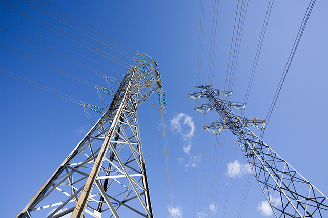 Kaksi voimajohtojen pylvästä, taustalla sinistä taivasta.