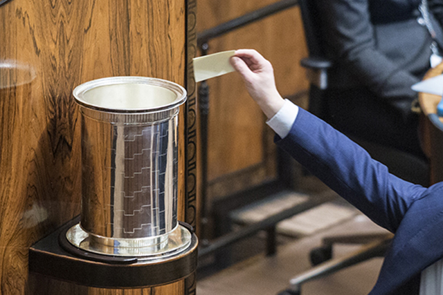 Käsi laittamassa äänestyslippua uurnaan istuntosalissa suljetussa lippuäänestyksessä