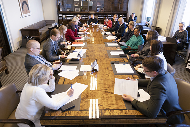 Sosiaali- ja terveysvaliokunta istumassa kokoushuoneessaan pitkän pöydän ympärillä. Jäsenet tutkivat pöydällä olevia papereita.