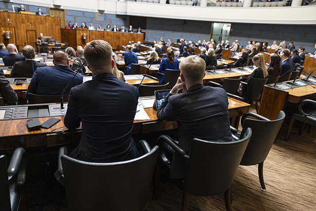 ihmisiä täysistuntosalissa istumassa selin kameraan