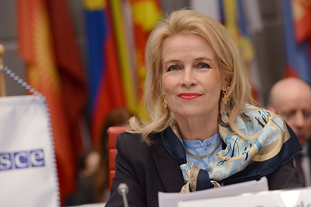 Pia Kauma kokoustilanteessa, taustalla värikäs lippurivistö.