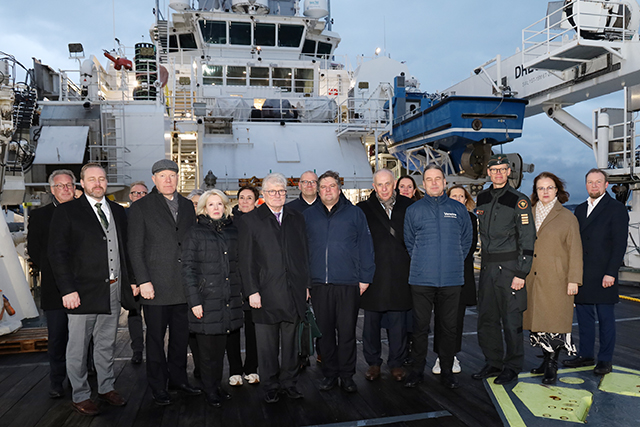 Kuvassa joukko ihmisiä pimentyvässä illassa rajavartiolaitoksen laivan edustalla.