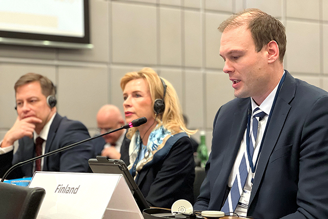 Suomen edustajia istumassa kokouksessa: Kaunisto puhuu mikrofoniin etualalla, taustalla Kauma ja Junnila